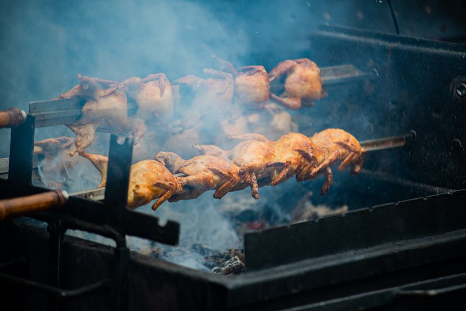 Juicy whole chickens roasting on a spit over open flames outdoors, creating smoky flavors.